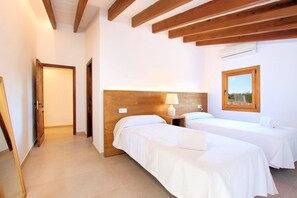 A hotel room with two beds, wooden beams on the ceiling, a window with a view, and a door leading to another room. - Finca Casou | Pollensa | Spacious countryside retreat with pool for. (Pollensa)