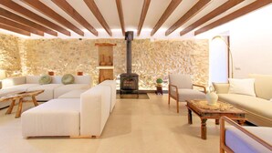 A cozy living room with a stone wall, a fireplace, and modern furniture. - Finca Casou | Pollensa | Spacious countryside retreat with pool for. (Pollensa)