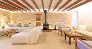 A cozy living room with a stone wall, a fireplace, and modern furniture. - Finca Casou | Pollensa | Spacious countryside retreat with pool for. (Pollensa)