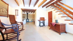 A hallway with wooden beams, a staircase, rocking chairs, a sewing machine, and a lamp on a table. - Finca Casou | Pollensa | Spacious countryside retreat with pool for. (Pollensa)