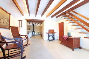 A hallway with wooden beams, a staircase, rocking chairs, a sewing machine, and a lamp on a table. - Finca Casou | Pollensa | Spacious countryside retreat with pool for. (Pollensa)