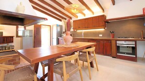 A kitchen with wooden cabinets, a dining table, chairs, a vase with flowers, and a hanging light fixture. - Finca Casou | Pollensa | Spacious countryside retreat with pool for. (Pollensa)