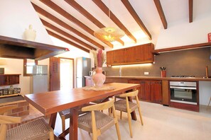 A kitchen with wooden cabinets, a dining table, chairs, a vase with flowers, and a hanging light fixture. - Finca Casou | Pollensa | Spacious countryside retreat with pool for. (Pollensa)