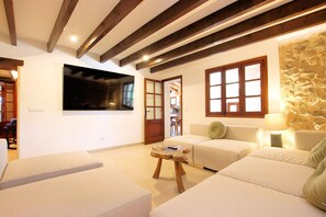 A modern living room with a large flat-screen TV mounted on the wall, a wooden coffee table, and a beige sofa. - Finca Casou | Pollensa | Spacious countryside retreat with pool for. (Pollensa)