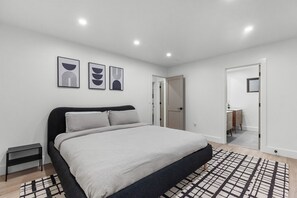 A modern bedroom with a large bed, a bedside table, and a nightstand. There are three framed artworks on the wall and a door leading to another room. - Hot tub, Game Room, Sleeps 16, No neighbors, Near Palisades, Woods (Truckee)