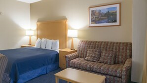 A hotel room with a bed, a sofa, a table, and two bedside lamps. - Hotel in Millinocket Maine with pool, lounge, food & Snowmobile/ATV trail access (Millinocket)