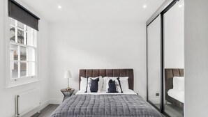 Een moderne slaapkamer met een groot bed, een nachtkastje, een lamp en uitzicht door een glazen deur.