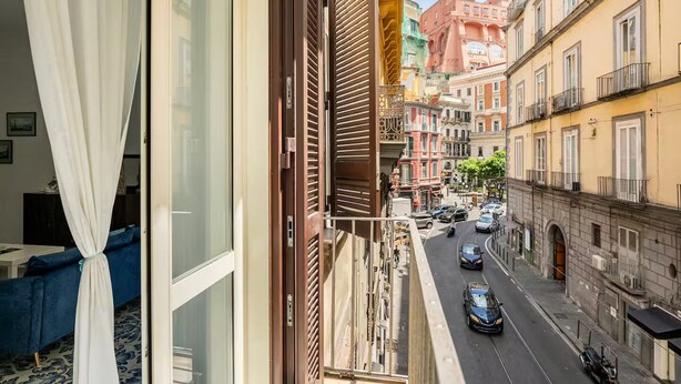 A balcony with a view of a street, a window with a curtain, and a blue sofa. - Ammore A Mare - Luxury Apartment Near The Sea (Napoli)