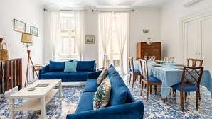 A living room with a blue sofa set, a dining table with chairs, and a patterned floor. - Ammore A Mare - Luxury Apartment Near The Sea (Napoli)