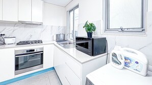 A modern kitchen with white cabinets, a stove, oven, sink, and a window with a view. - 1BR Granny Flat / Free Parking / Near Airport & Train (Arncliffe)