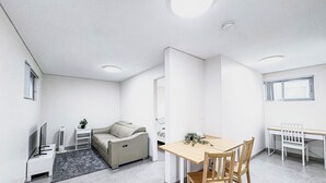 A modern, minimalist living room with a sofa, a dining table, and a TV. - 1BR Granny Flat / Free Parking / Near Airport & Train (Arncliffe)