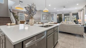 A modern kitchen with a large island, stainless steel appliances, pendant lighting, and a neutral color palette. - 2332 Distant Sun Trail (Kissimmee)