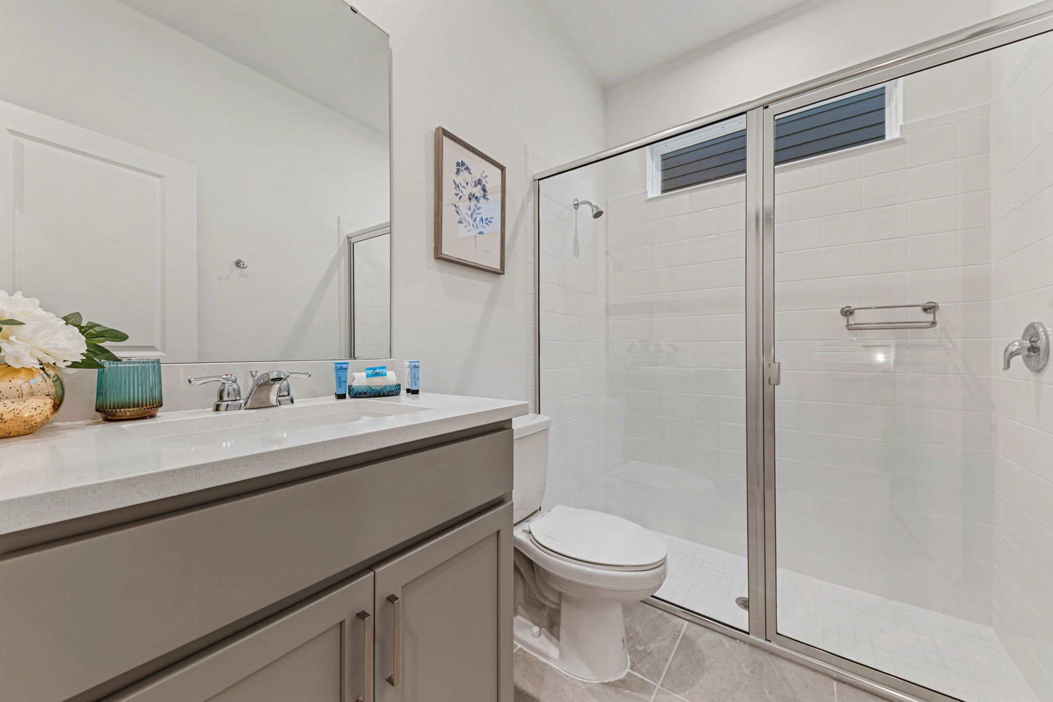 A modern bathroom with a glass shower enclosure, a white toilet, and a vanity with a mirror and a vase of flowers.