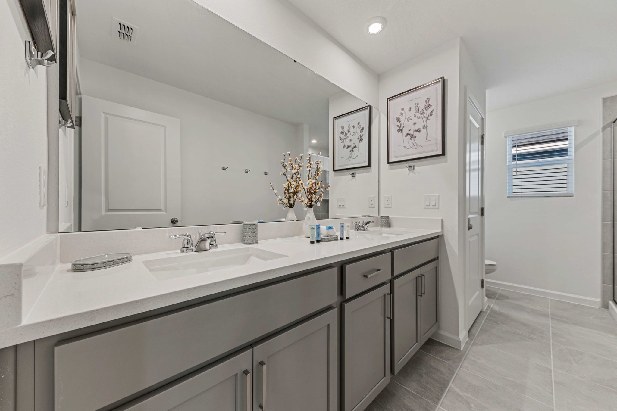 A modern bathroom with a large mirror, two sinks, and a vanity with cabinets.