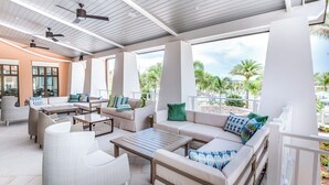 A spacious outdoor lounge area with multiple seating options, ceiling fans, and large windows offering views of palm trees and a beach. - 2332 Distant Sun Trail (Kissimmee)