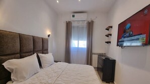 Une chambre à coucher avec un grand lit, un téléviseur fixé au mur et une fenêtre avec des rideaux.