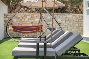 A poolside area with lounge chairs, a hammock, and a stone wall.
