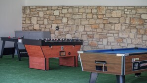 Una mesa de billar y dos mesas de futbolín en un cuarto con pared de piedra.