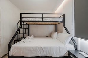A bunk bed with a white mattress and pillows, a wooden ladder, and a small bedside table with a remote control.