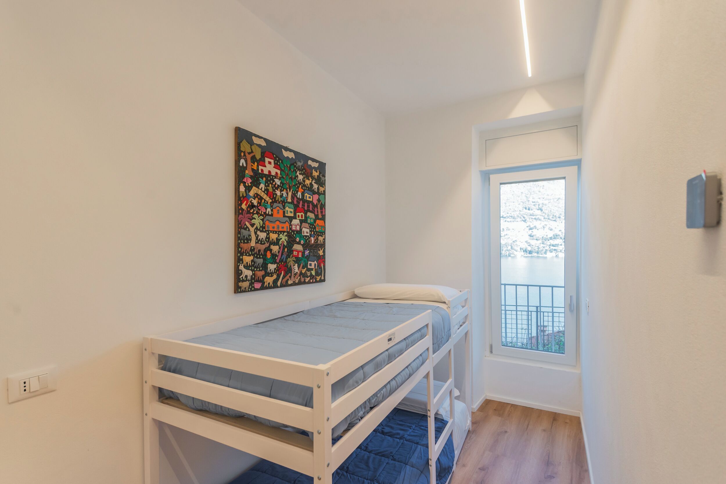 Ein kleines Zimmer mit einem Etagenbett, einem Fenster mit Blick auf eine verschneite Landschaft und einem farbenfrohen Wandgemälde.