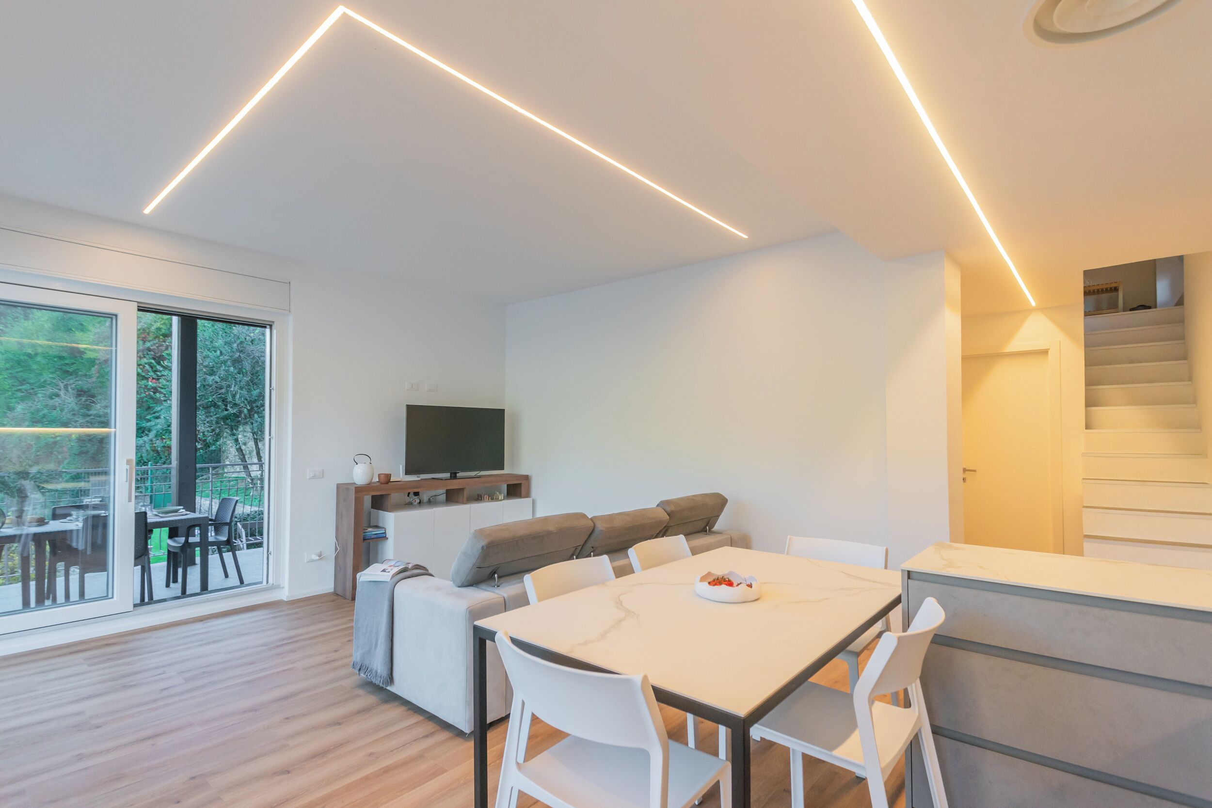 Uma sala de estar moderna com uma mesa de jantar, cadeiras brancas, um sofá e uma televisão.