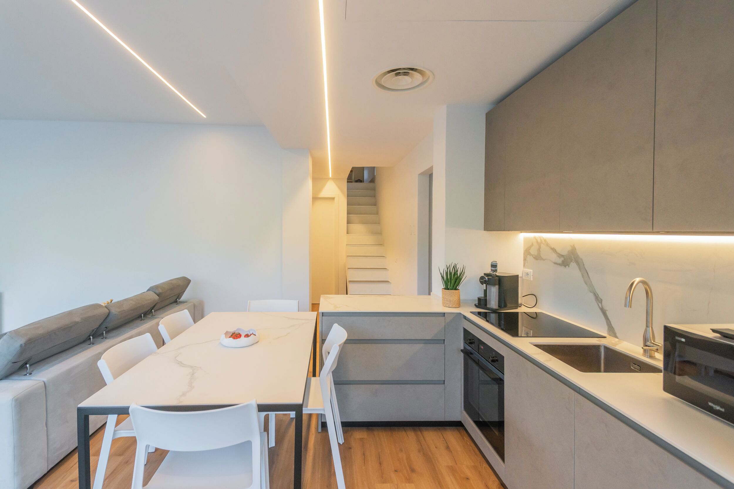 A modern kitchen with a central island, built-in appliances, and a staircase leading to an upper level.