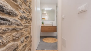 A hallway with a stone wall, a wooden floor, a gray rug, a white sink, and a mirror. - Villa Regina Retreat With Pool & Lake View (Brienno)