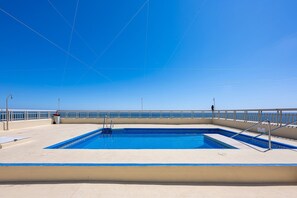 En klarblå himmel, en pool med trappsteg och ett räcke med utsikt över en vattenyta.