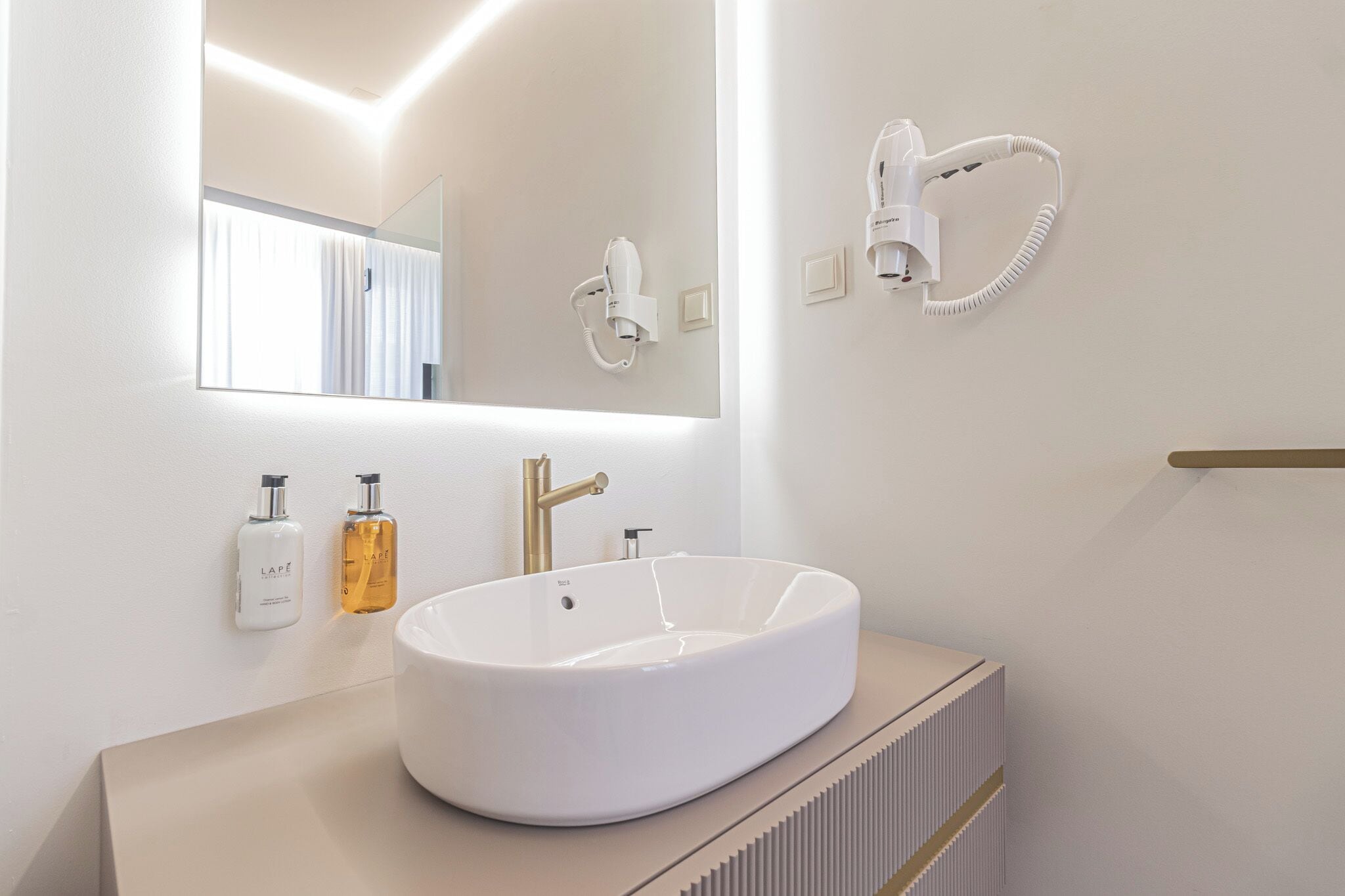 A modern bathroom with a large mirror, a white sink, and a hairdryer mounted on the wall.