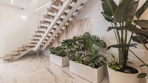 A modern staircase with glass railings and white steps, surrounded by potted plants and a marble floor. - Galega Villas (Mafra)
