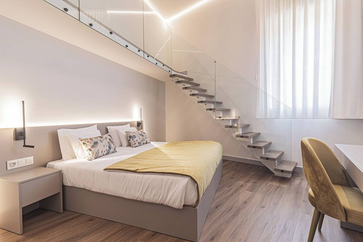 A modern bedroom with a bed, bedside table, and a staircase leading to an upper level.
