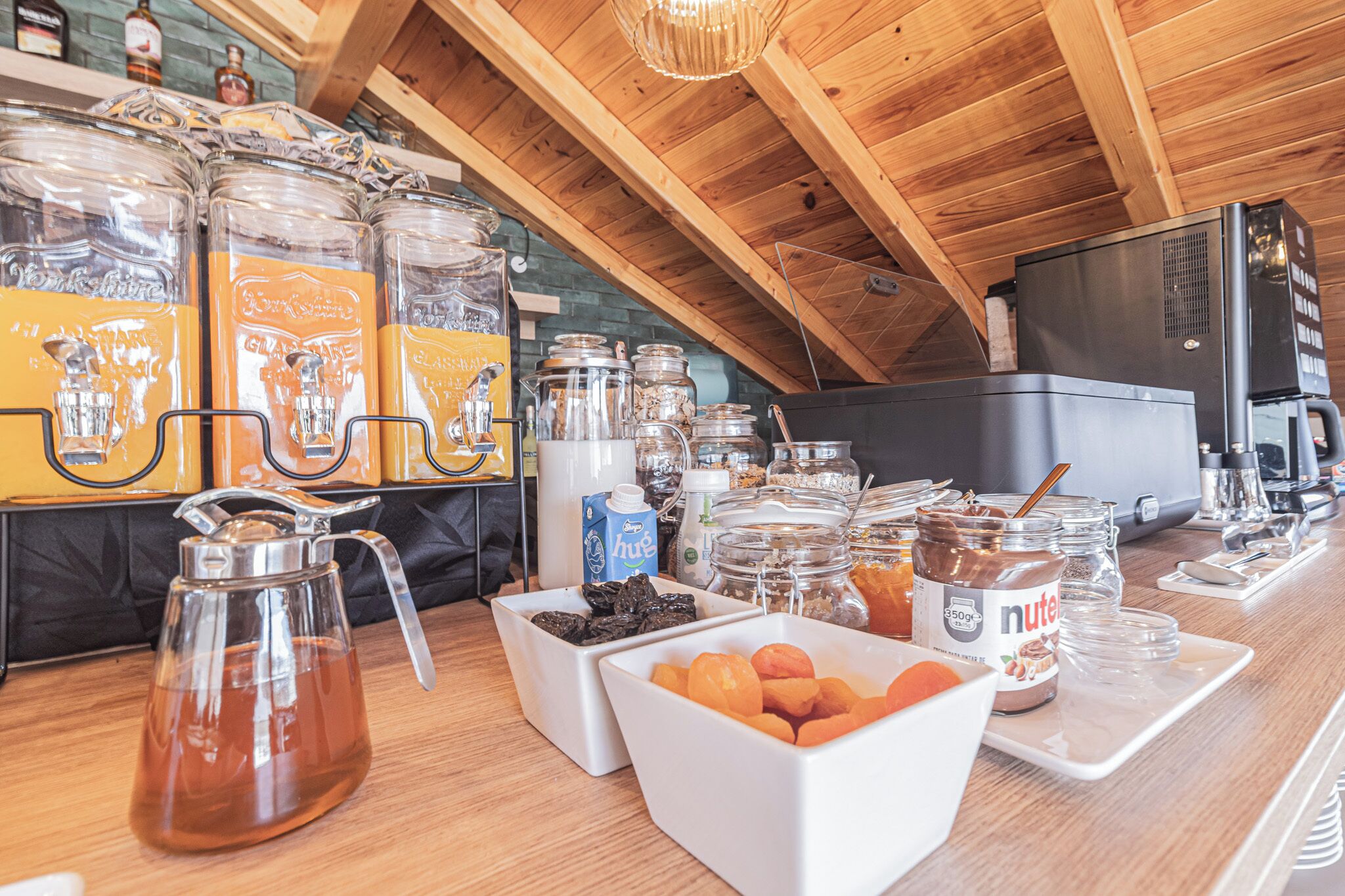 A breakfast buffet with various food items and beverages, including jars of honey, jars of marmalade, and a coffee machine.