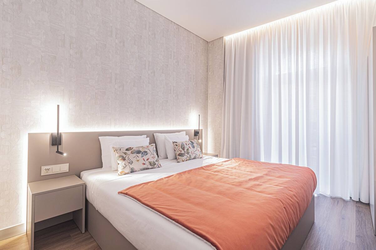 A modern hotel room with a large bed, a nightstand, and a wall-mounted light.