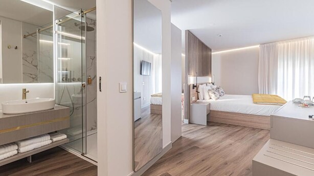 A modern hotel room with a large mirror, a built-in sink, a bed with a wooden headboard, and a bedside table. - Galega Villas (Mafra)