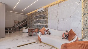 A modern living room with a curved white sofa, orange cushions, a marble coffee table, and a patterned wall. - Galega Villas (Mafra)