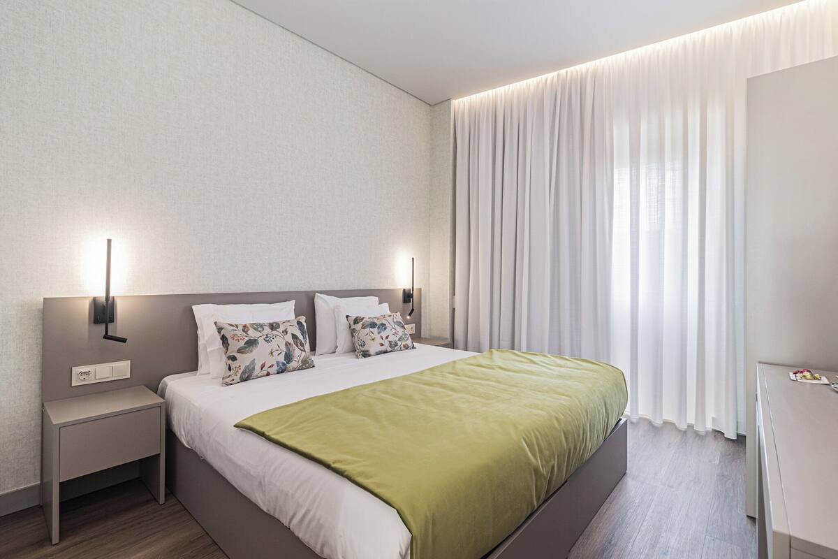 A modern hotel room with a large bed, two bedside tables, a nightstand, and a desk.