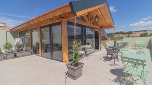 A covered outdoor area with a wooden roof, glass walls, and outdoor seating. - Galega Villas (Mafra)