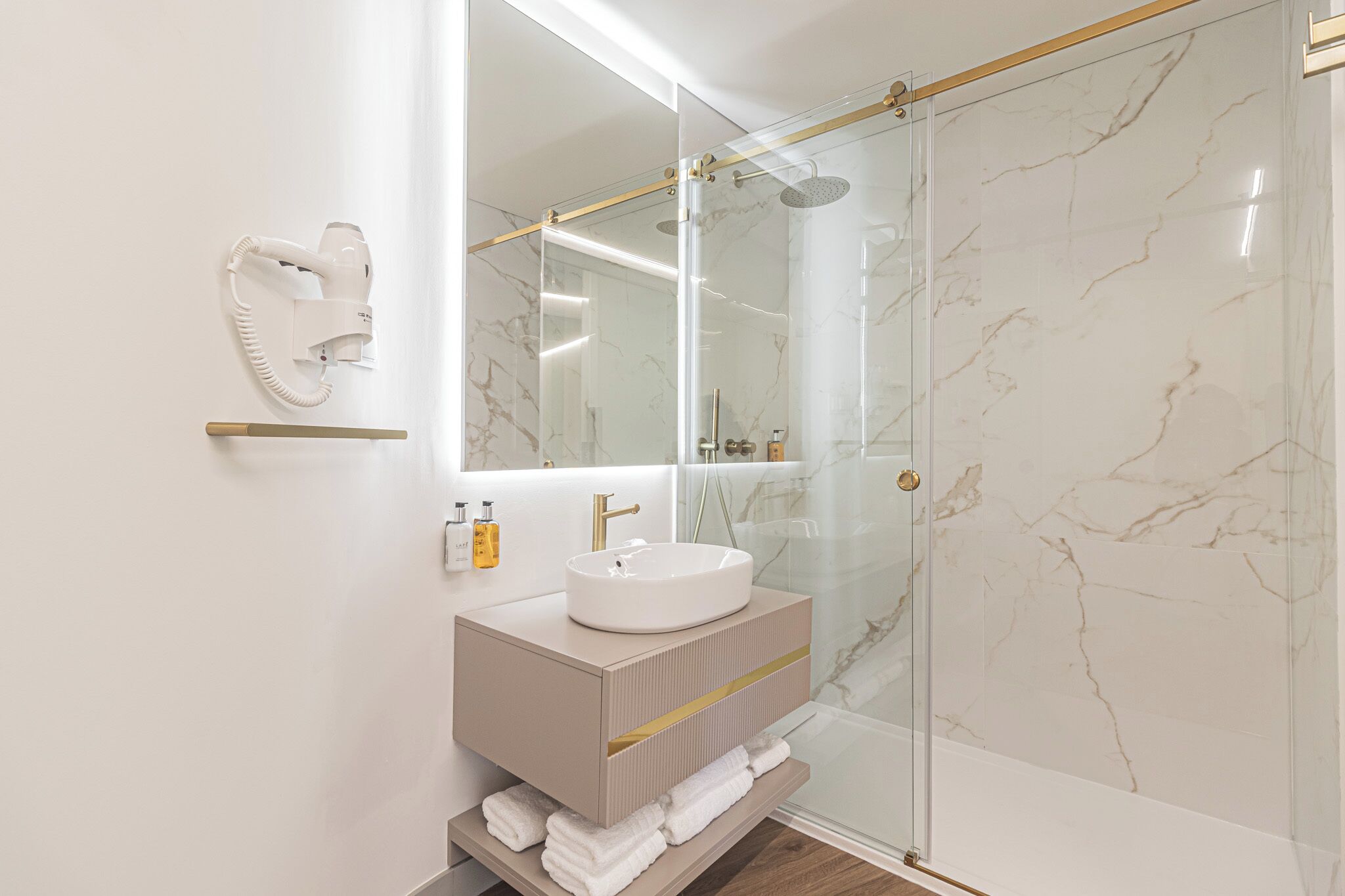 Un baño moderno con ducha de vidrio, lavamanos blanco y tocador con espejo.