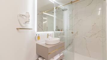 Un baño moderno con ducha de vidrio, lavamanos blanco y tocador con espejo.