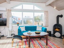 Una sala de estar acogedora con un sofá azul, una mesa redonda de centro, una chimenea y un ventanal grande.