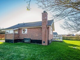 Una casa de ladrillo con chimenea, una ventana y un banco en el patio.