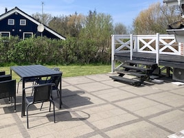 Un patio exterior con una mesa y sillas, una terraza de madera y un edificio al fondo.