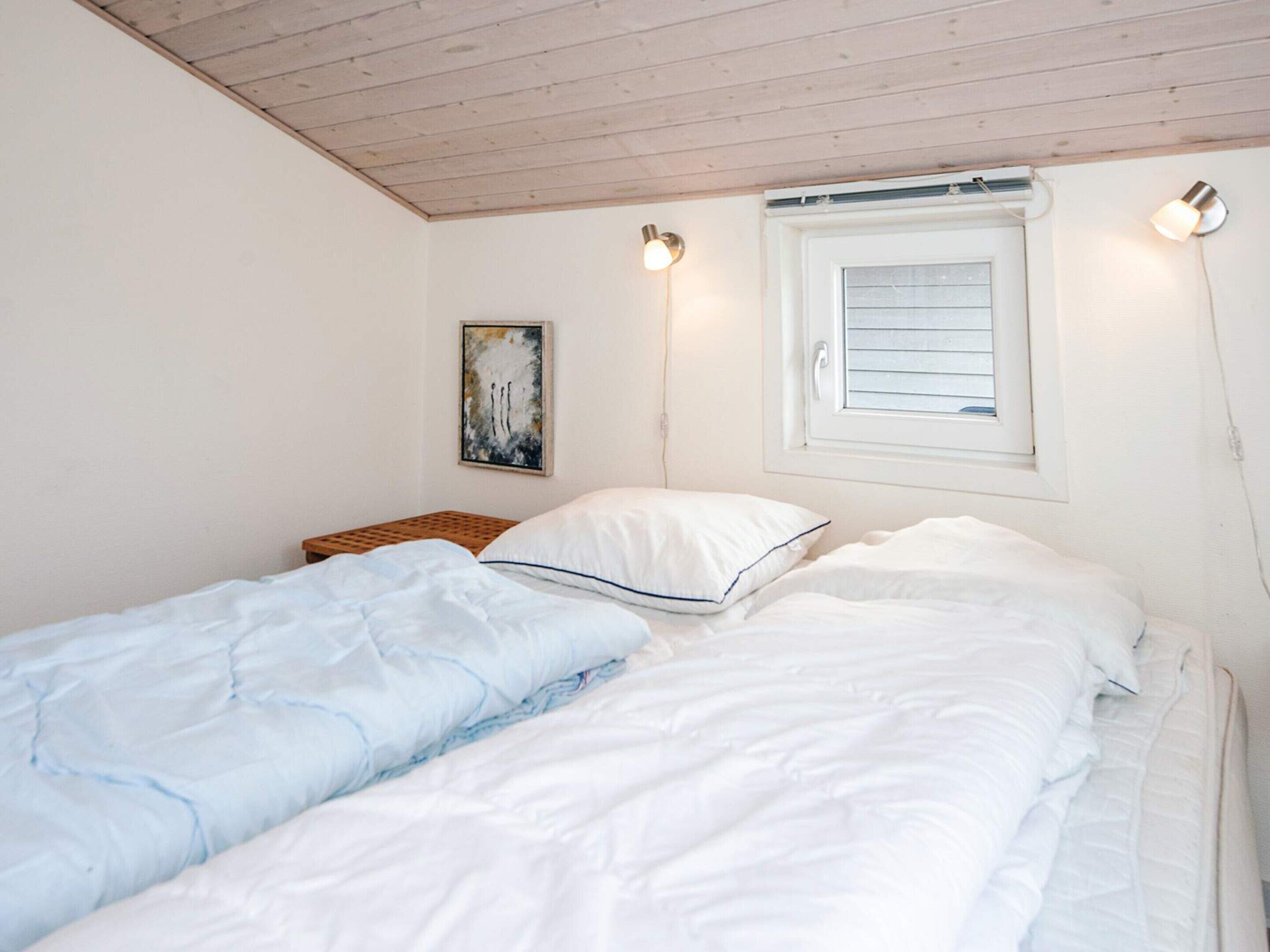 A bedroom with two single beds, a wooden ceiling, a window with blinds, a wall-mounted light, and a painting.