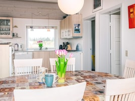 Una cocina moderna con armarios blancos, una mesa de comedor con mantel antiguo y un florero con tulipanes.
