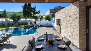 Un espace extérieur avec une piscine, des chaises longues, une table à manger pour deux personnes et un mur en briques.