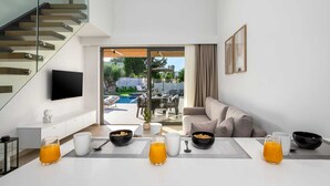 Un salon moderne doté d’un escalier en verre, d’un téléviseur à écran plat, d’un coin repas avec une table préparée pour le petit-déjeuner, et offrant une vue sur la piscine extérieure et le jardin.