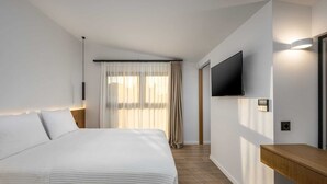 Une chambre d’hôtel moderne dotée d’un grand lit, d’un téléviseur à écran plat fixé au mur et d’une table de chevet en bois.