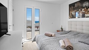 A bedroom with a bed, a TV, a painting, and a door leading to a balcony. - Holiday Home 'Casa Do Cabeco' with Sea View and Wi-Fi (Cabeco de Ponta)