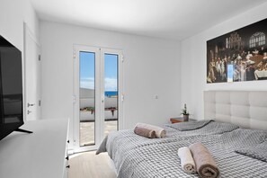 A bedroom with a bed, a TV, a painting, and a door leading to a balcony.