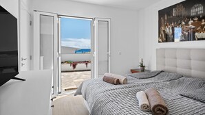 A bedroom with a bed, a TV, a painting, and a balcony with a view. - Holiday Home 'Casa Do Cabeco' with Sea View and Wi-Fi (Cabeco de Ponta)